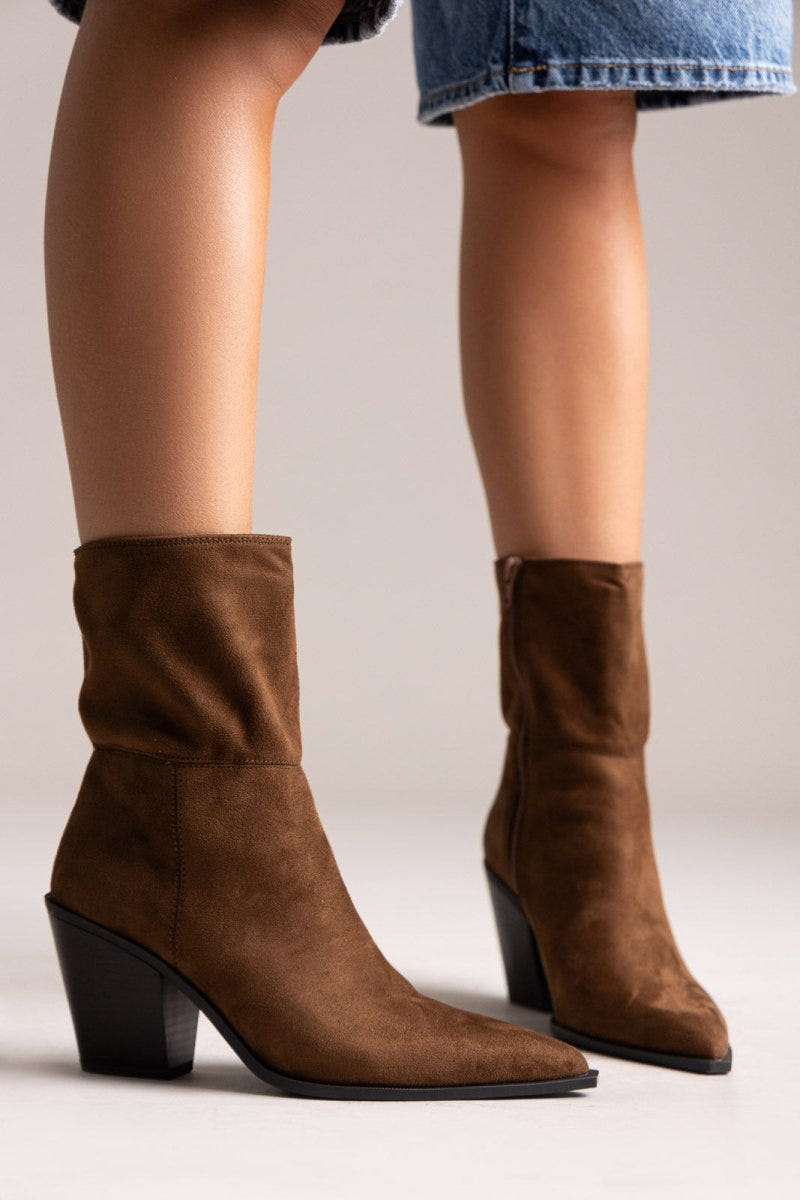 Model legs in dark brown suede pointed ankle boots with block heels and slouched shafts, front view on a light backdrop