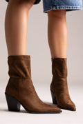 Model legs in dark brown suede pointed ankle boots with block heels and slouched shafts, front view on a light backdrop