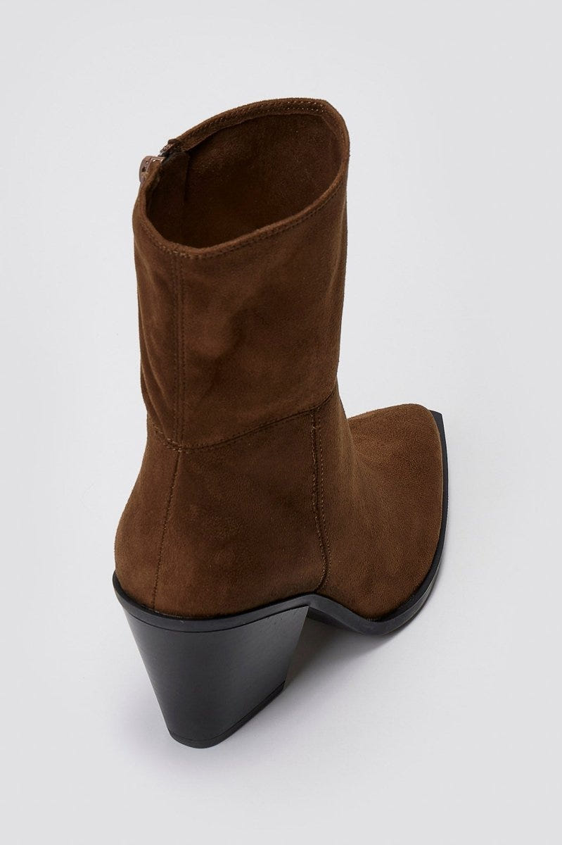 Dark brown suede pointed ankle boot with block heel and slouched shaft, angled overhead view on a light grey background