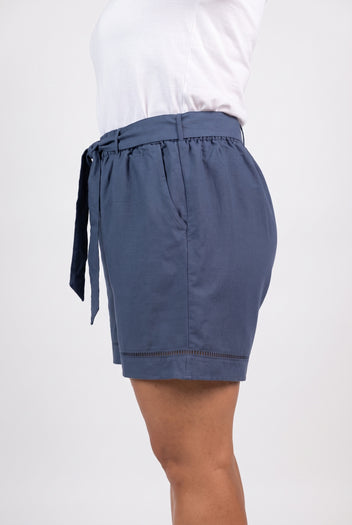 Model wearing dark blue linen blend shorts with tie belt and lace trim hem, side view with white t-shirt