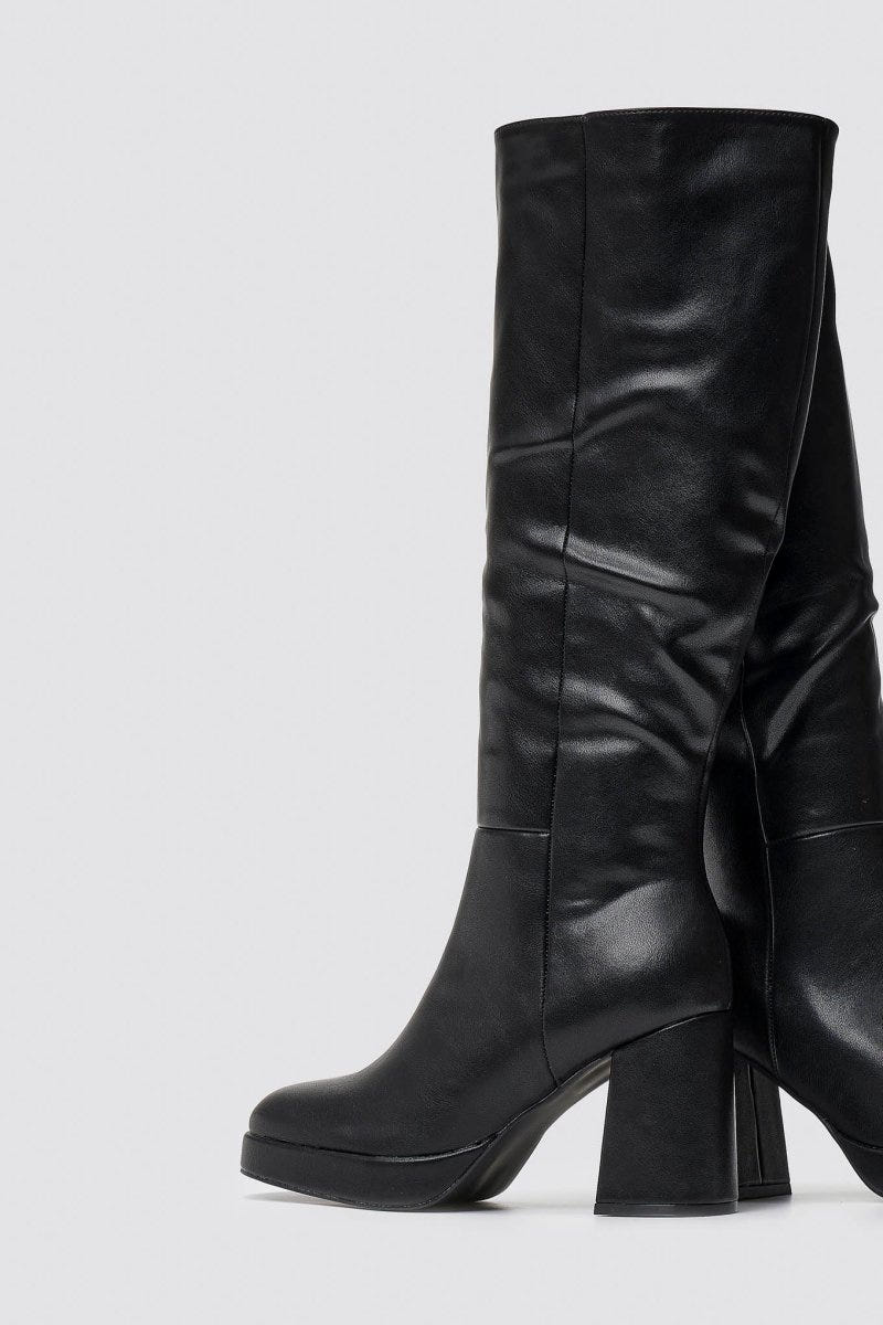 Close-up of black leather knee-high boot with smooth shaft, platform sole and block heel worn by a model