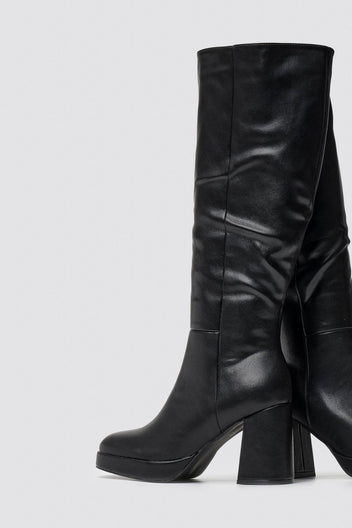 Close-up of black leather knee-high boot with smooth shaft, platform sole and block heel worn by a model