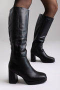 Model legs in black leather knee-high platform boots with block heels and sheer tights, three-quarter view