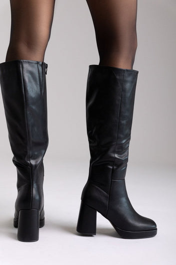 Model legs in black leather knee-high platform boots with block heels and sheer black tights, front view