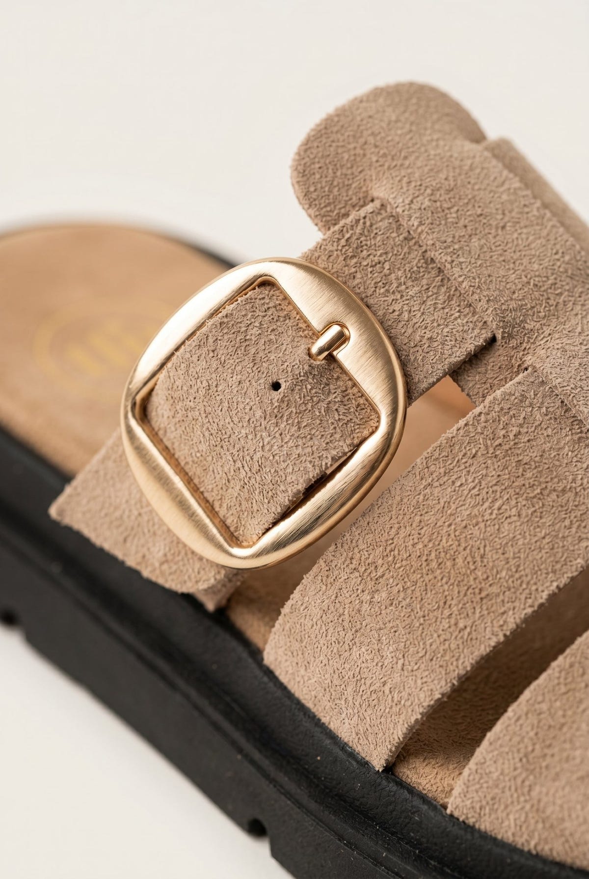 Close-up of beige suede fisherman slide sandal with large gold buckle on a chunky black sole