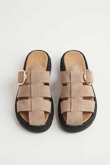 Overhead view of a pair of beige suede fisherman slide sandals with woven straps, gold buckles and black soles