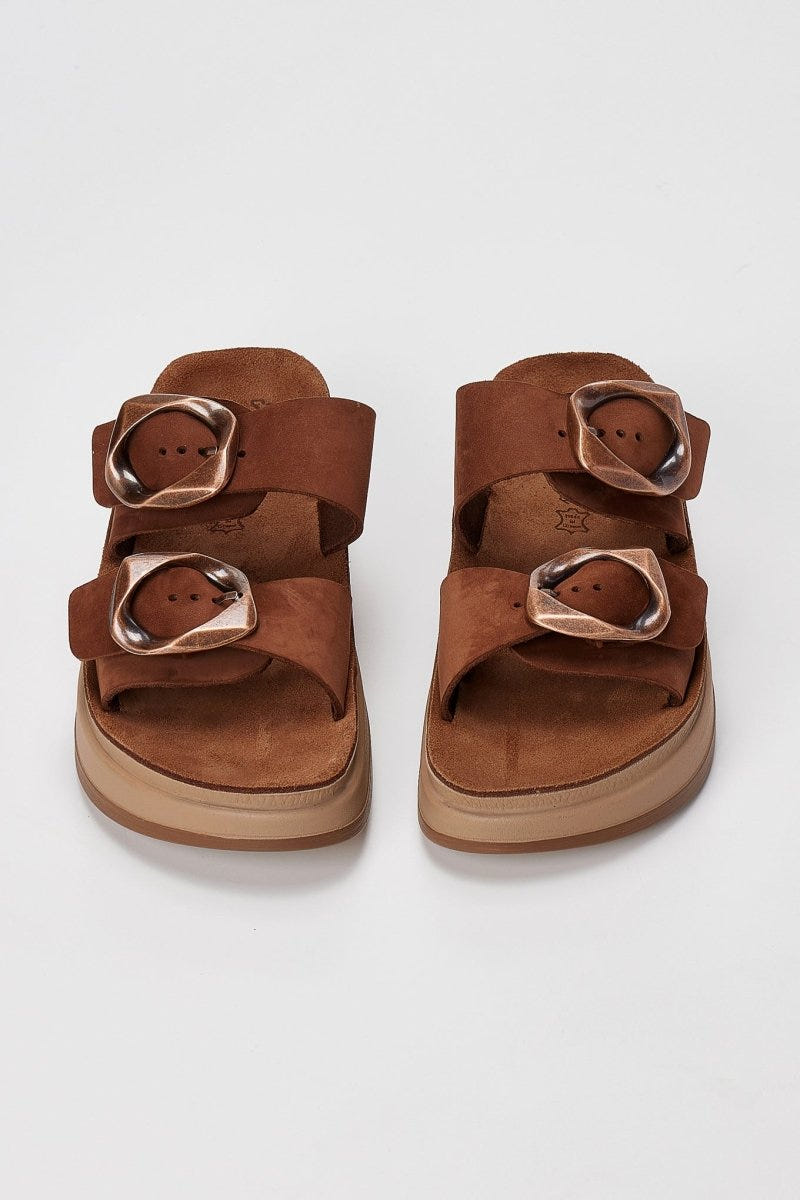 Pair of brown suede flatform sandals with two wide straps and round metallic buckles seen from above on light grey