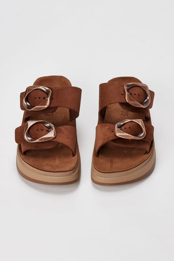 Pair of brown suede flatform sandals with two wide straps and round metallic buckles seen from above on light grey