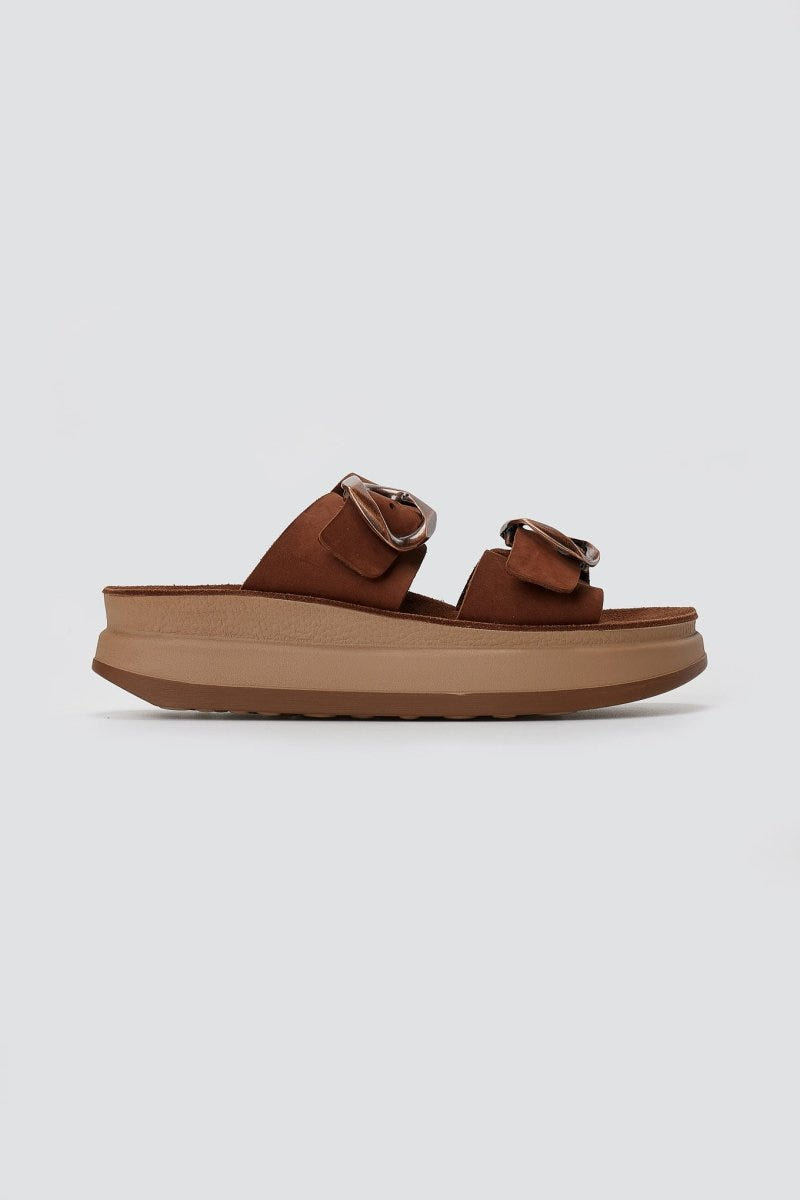Single brown suede flatform sandal with two straps and round silver buckles on thick tan platform sole, side view on light grey