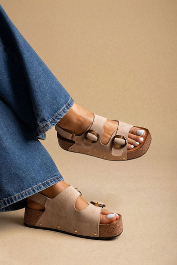 Model wearing taupe suede platform sandals with gold ring buckles and blue jeans, three-quarter view of feet