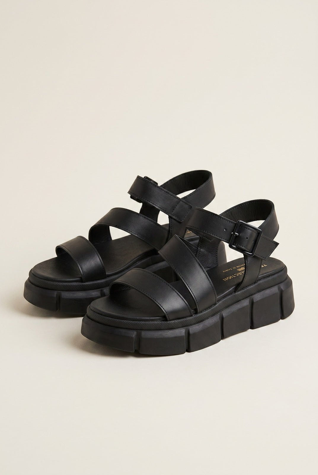 Pair of black leather flatform sandals with wide crossover straps, ankle buckle and chunky ridged soles, angled view