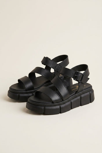Pair of black leather flatform sandals with wide crossover straps, ankle buckle and chunky ridged soles, angled view