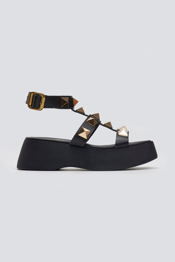 Black leather flatform sandal with gold pyramid studs, buckled ankle strap and thick platform sole, side view