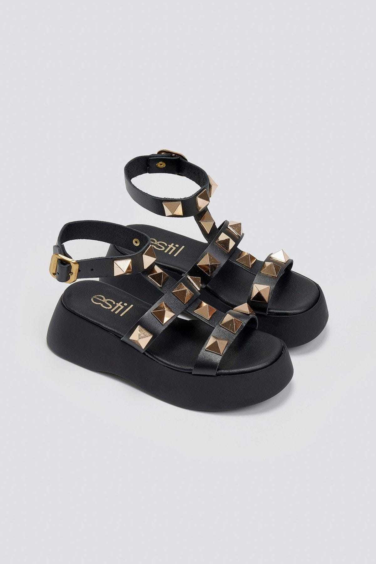 Black leather flatform sandals with gold pyramid studs, ankle straps with buckles and thick platform soles, angled view