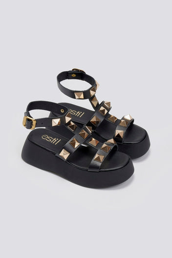 Black leather flatform sandals with gold pyramid studs, ankle straps with buckles and thick platform soles, angled view