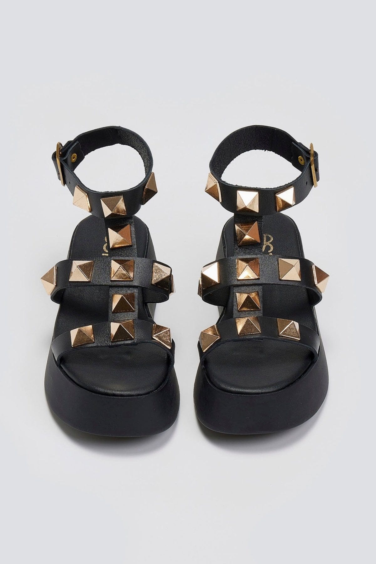 Overhead view of a pair of black leather flatform sandals with gold pyramid studs and buckled ankle straps