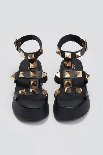 Overhead view of a pair of black leather flatform sandals with gold pyramid studs and buckled ankle straps
