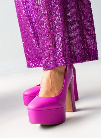 Fuchsia platform pumps with tall block heels and smooth rounded toes, worn on model, front three-quarter view.