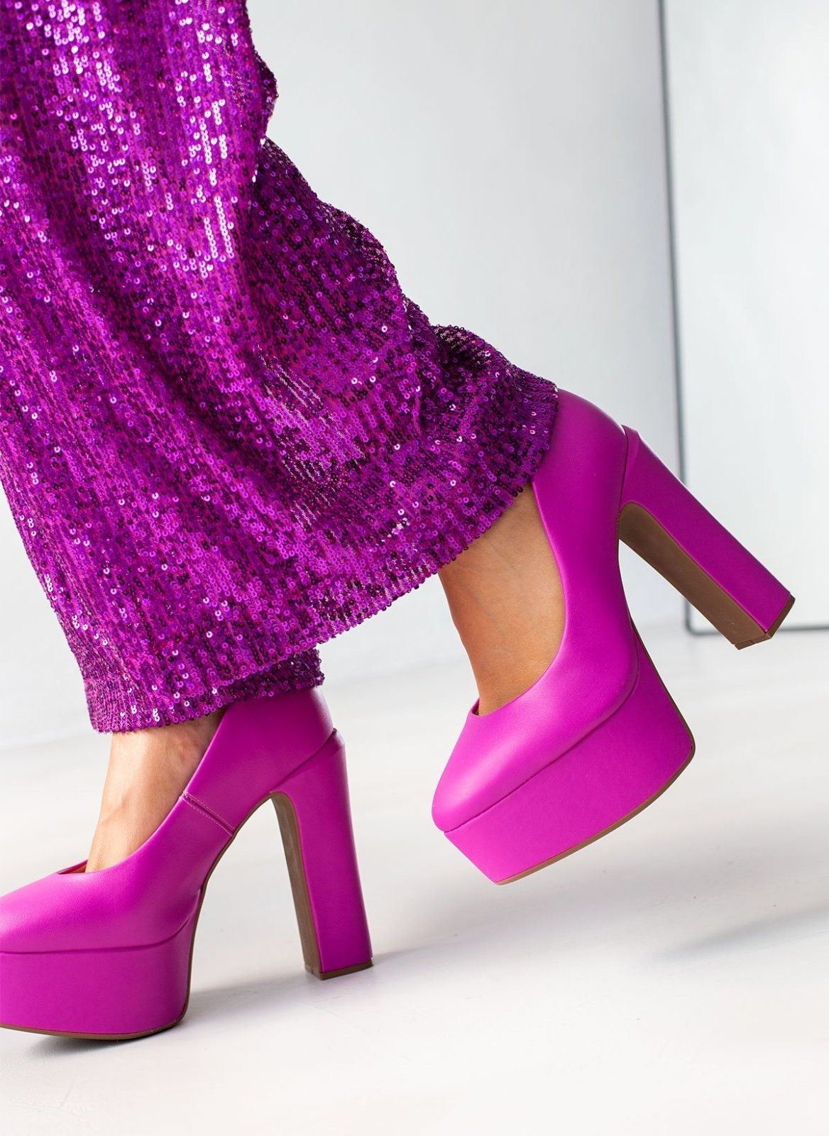 Fuchsia platform pumps with chunky block heels and rounded toes, worn on model, low angle side view.