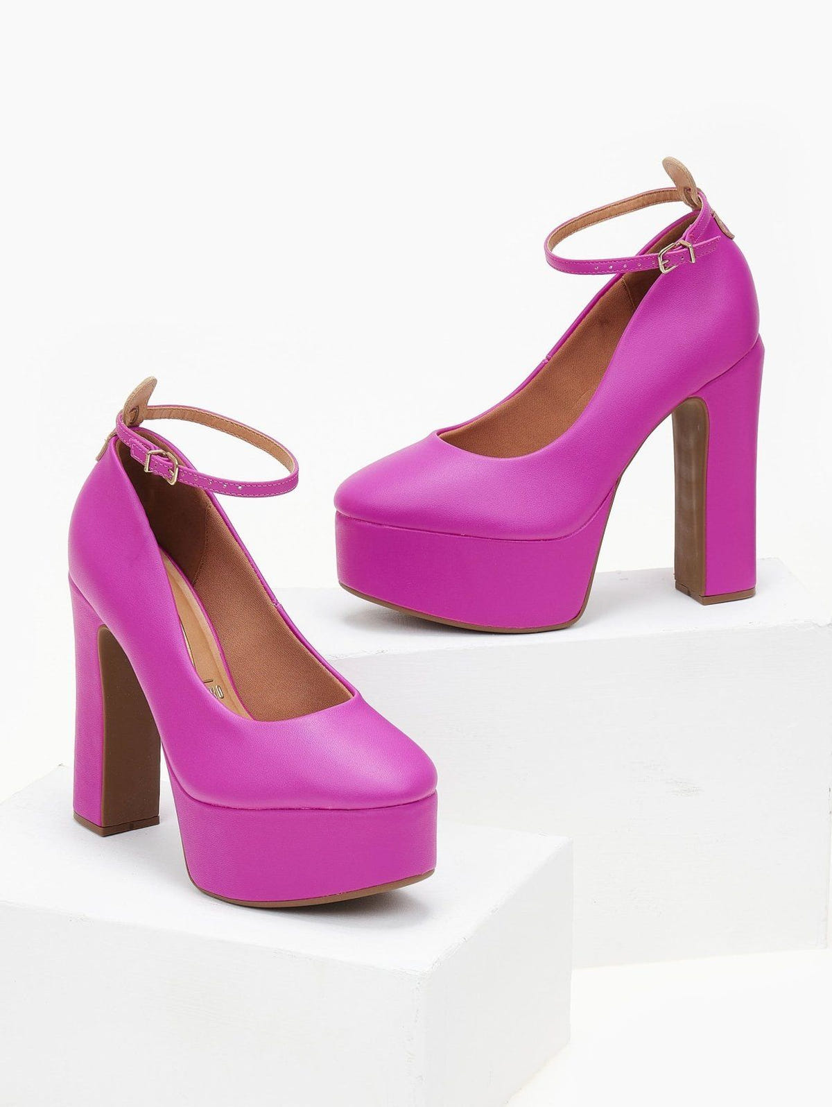Pair of fuchsia platform pumps with block heels and tan-lined ankle straps, shown on white blocks.