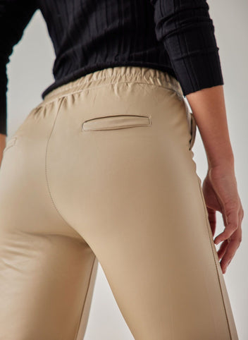 Beige faux leather leggings with elasticated waistband, back welt pocket and vertical seam down the leg, worn on model, back close-up