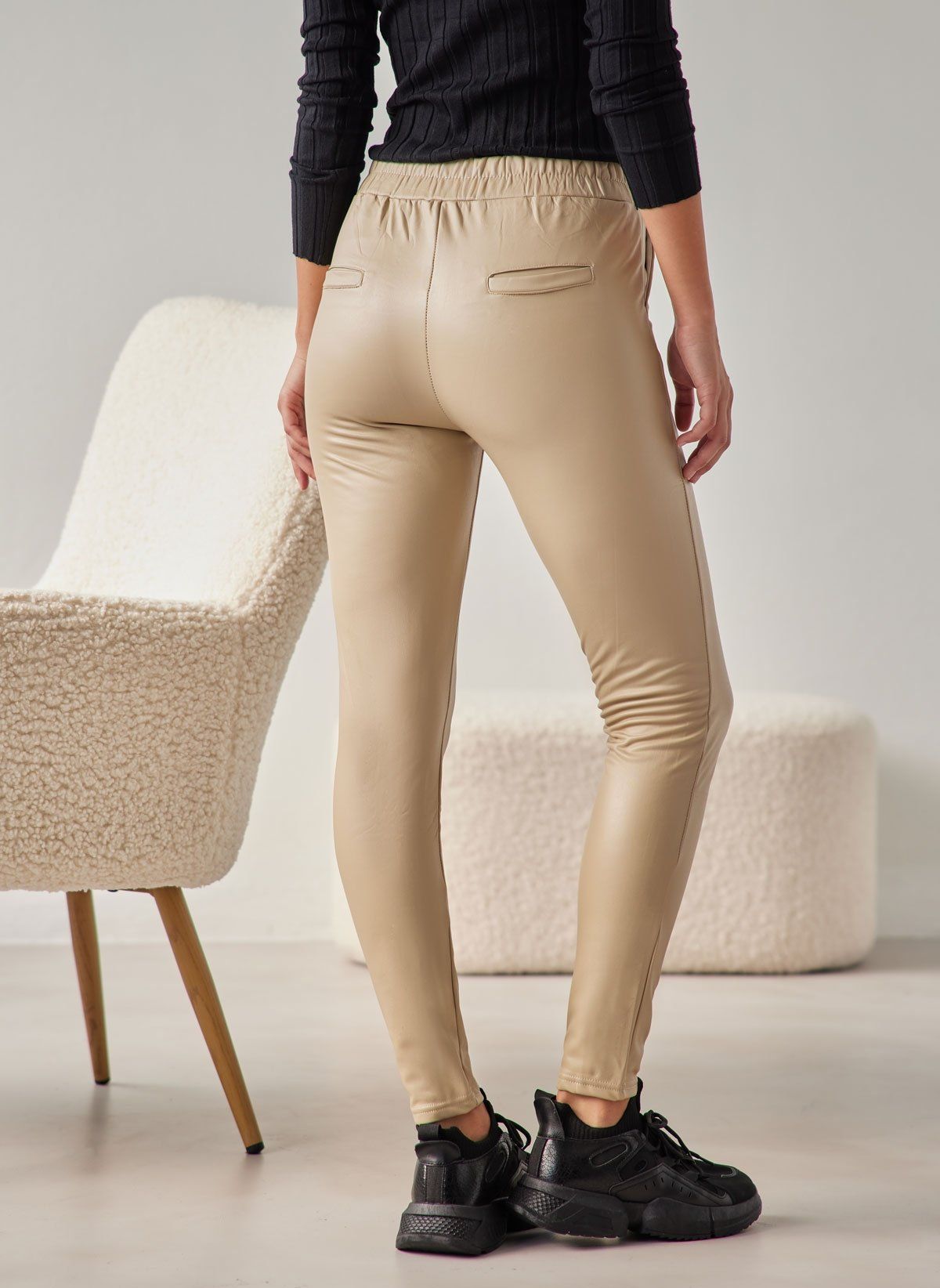 Beige faux leather leggings with elasticated waistband, back welt pockets and vertical side seam, worn on model, full-length back view