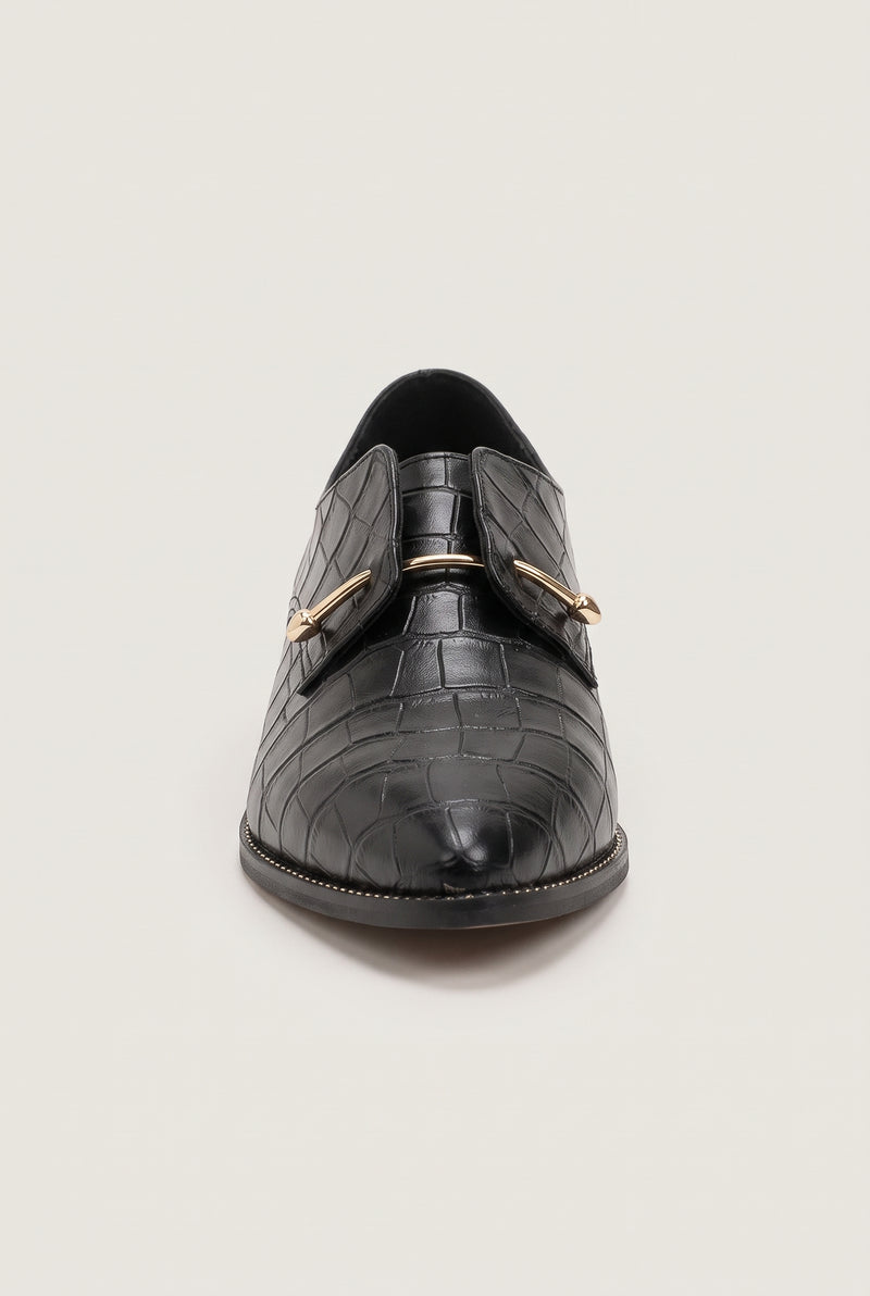 Front view of black croc-embossed pointed loafers highlighting the gold bar detail