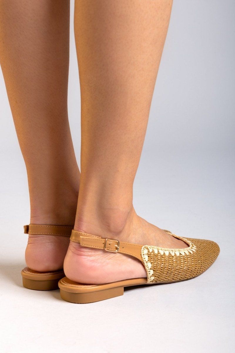 Rear view of model wearing tan woven raffia pointed toe slingback flats with cream trim and ankle straps