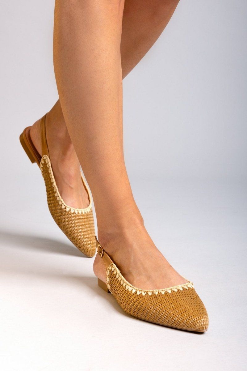 Model walking in tan woven raffia pointed toe slingback flats with cream trim and ankle straps