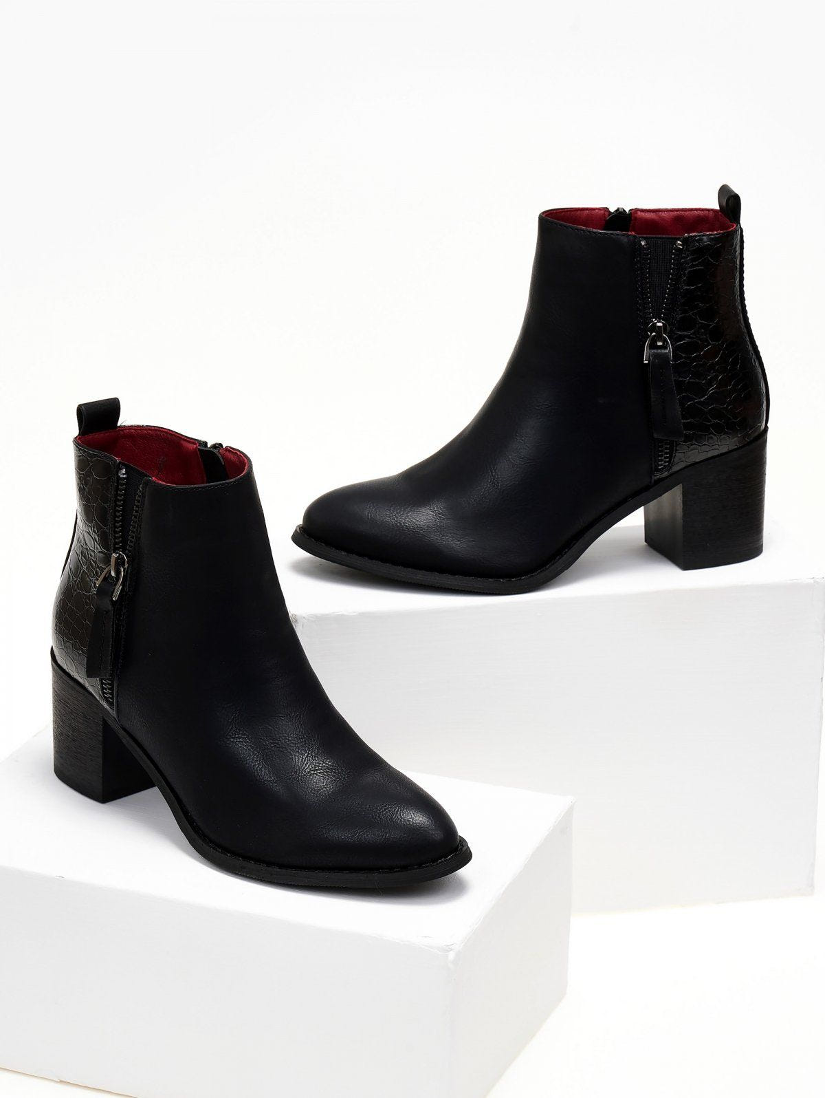 Black ankle boots with crocodile embossed panel and side zip with leather tassel, displayed on white blocks
