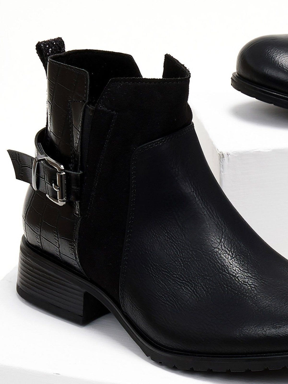 Close-up of black ankle boot with silver buckle, croc-embossed panel, suede insert and block heel