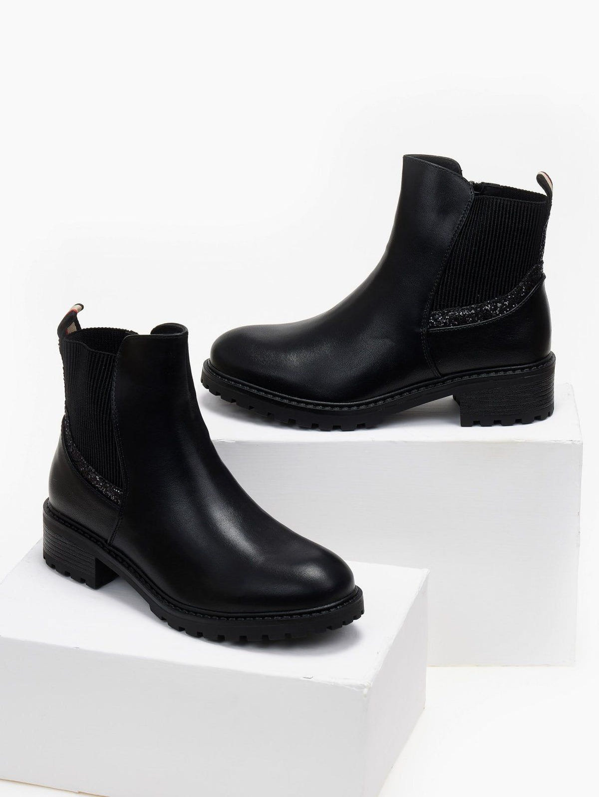Pair of black glitter-trim Chelsea ankle boots with low block heel and lug sole, displayed on white blocks