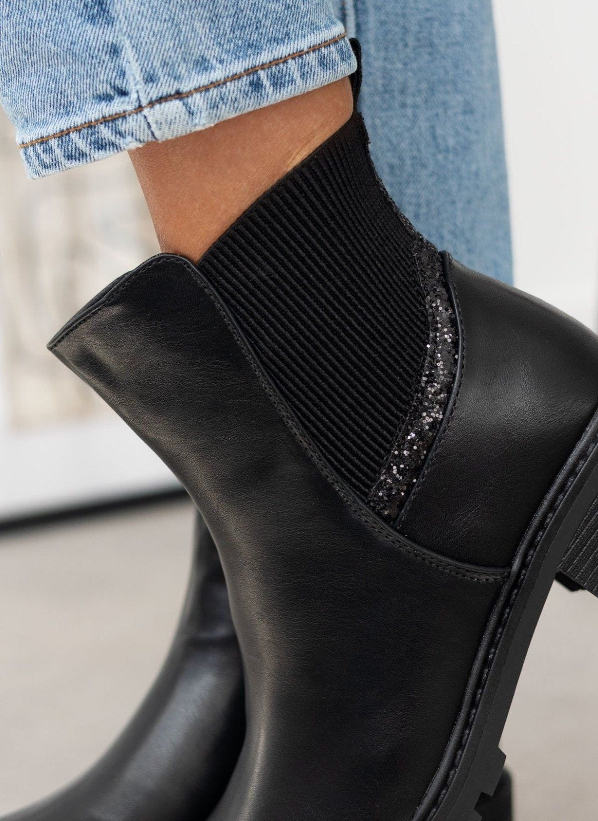 Close-up of black ankle boot ribbed elastic panel and glitter edging, worn on model