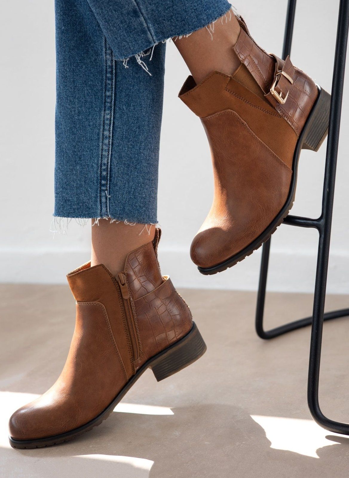 Tan faux leather ankle boot with gold buckle strap, croc-effect back and low block heel, worn on model, side view