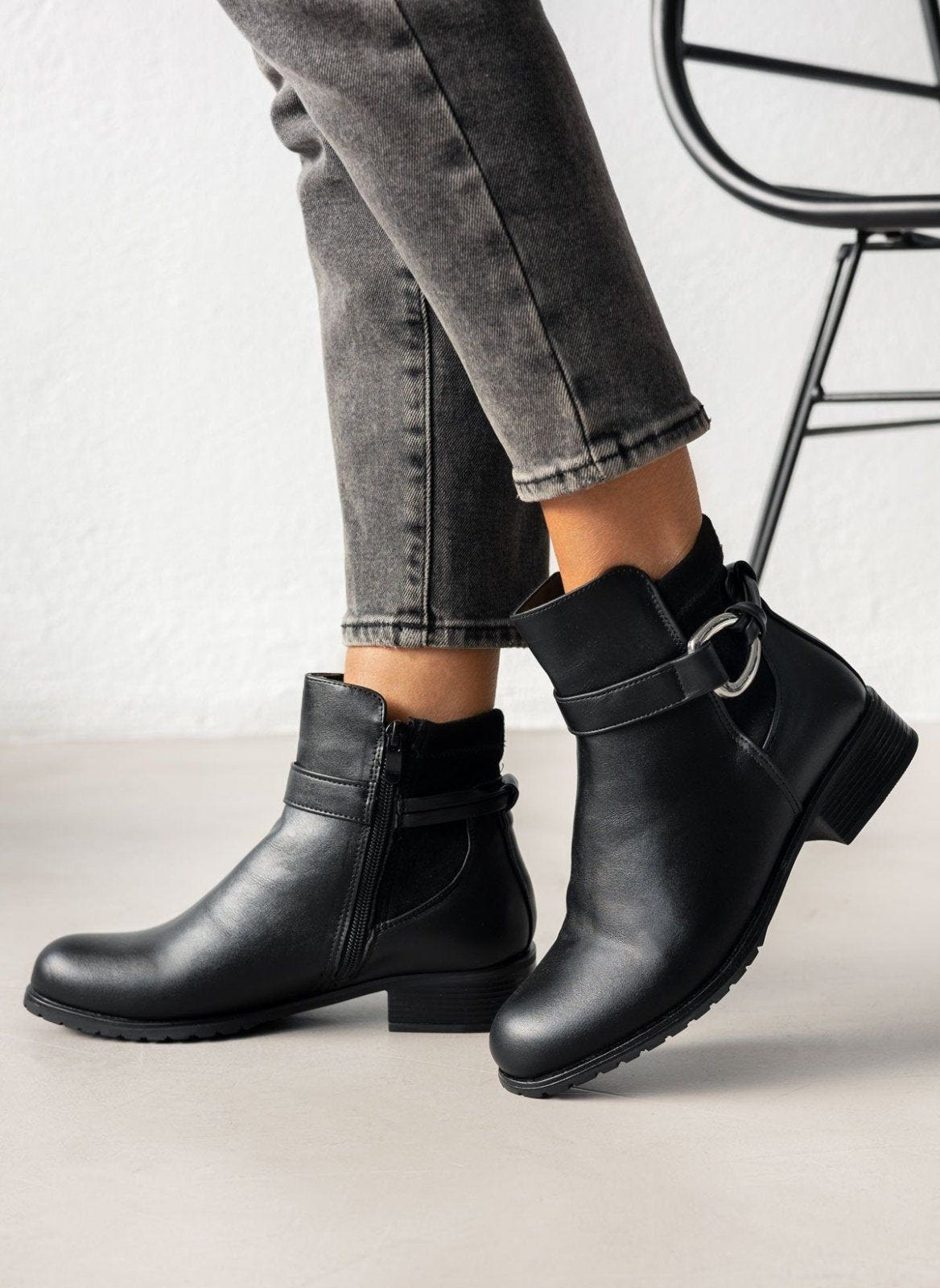 Black faux leather ankle boots with ankle strap, silver ring buckle and side zip, worn on model, front view