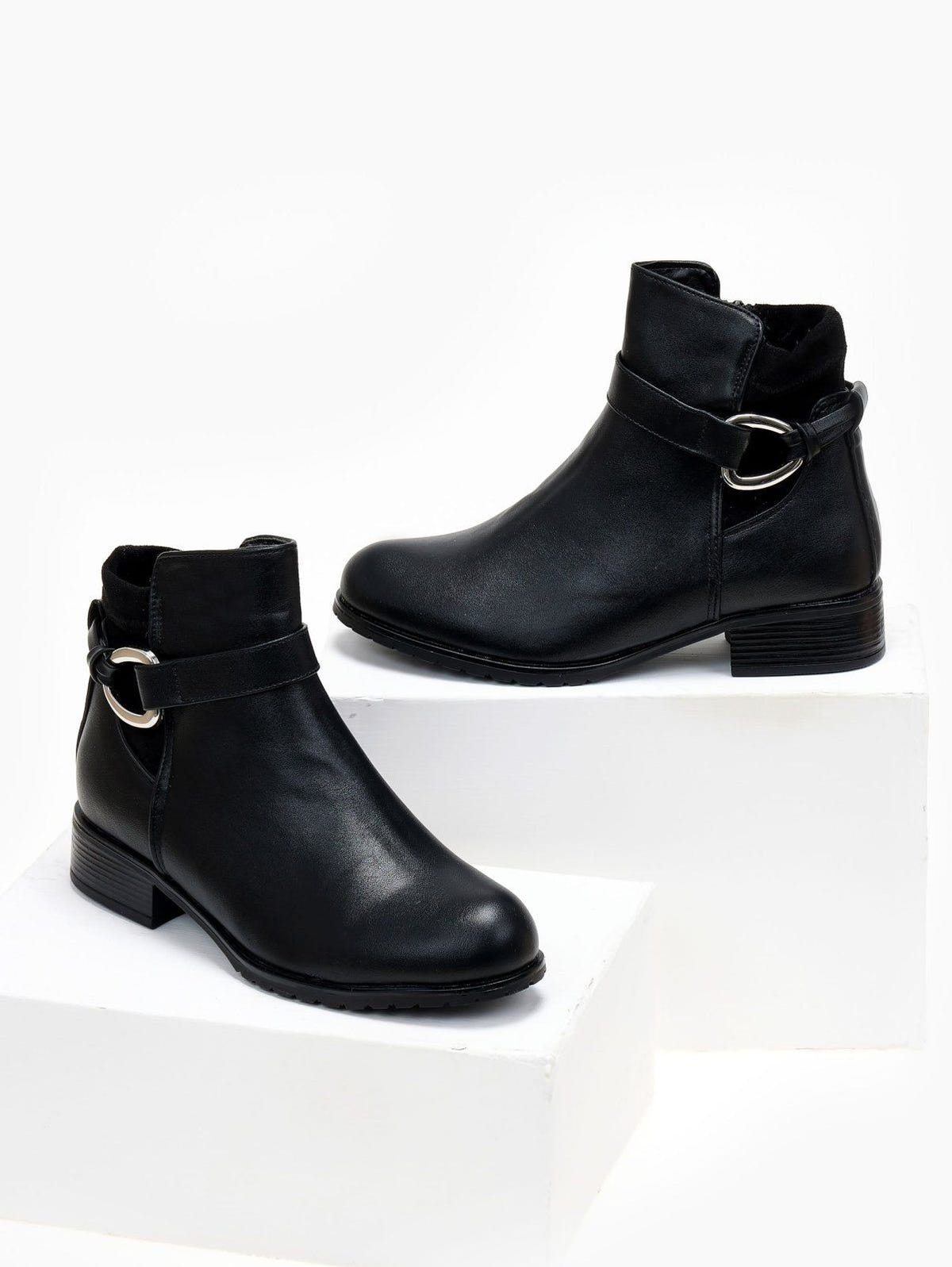 Black faux leather ankle boots with buckle strap, silver ring detail and low block heel, front view on white blocks