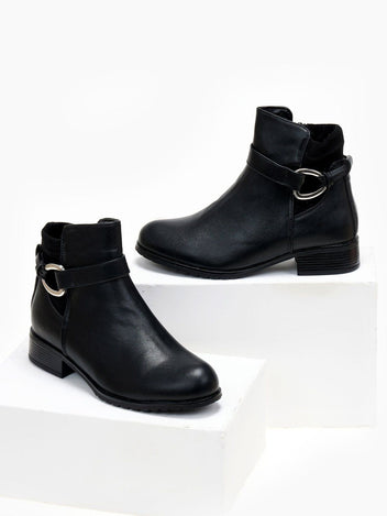 Black faux leather ankle boots with buckle strap, silver ring detail and low block heel, front view on white blocks