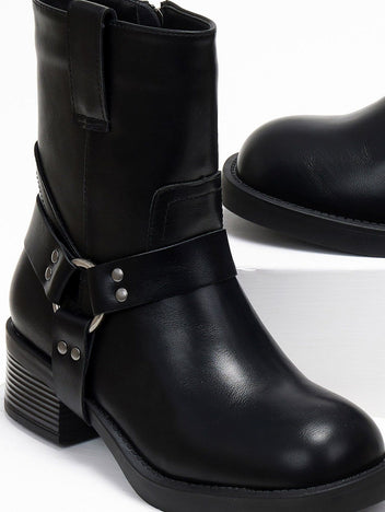Close-up of black faux leather biker boot with metal ring harness strap, studs and stacked block heel