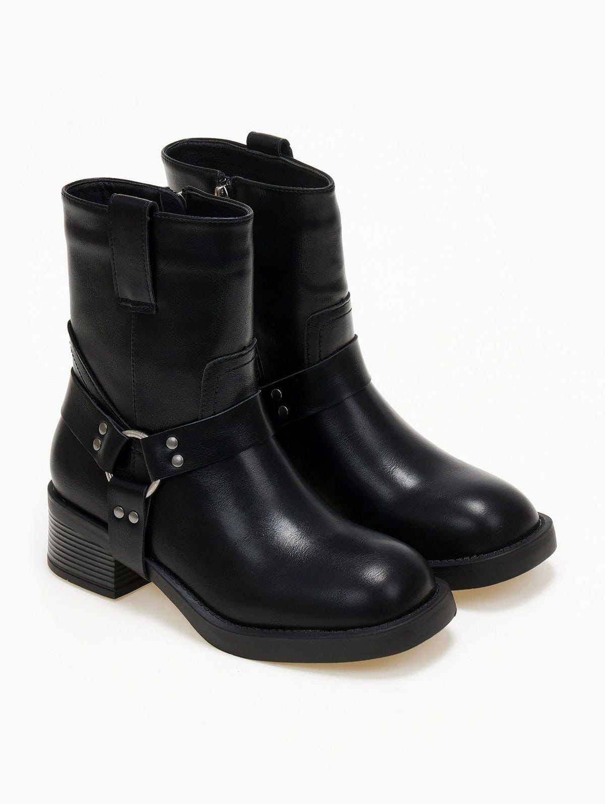 Pair of black faux leather biker boots with metal ring harness strap, studs and block heel, three-quarter view
