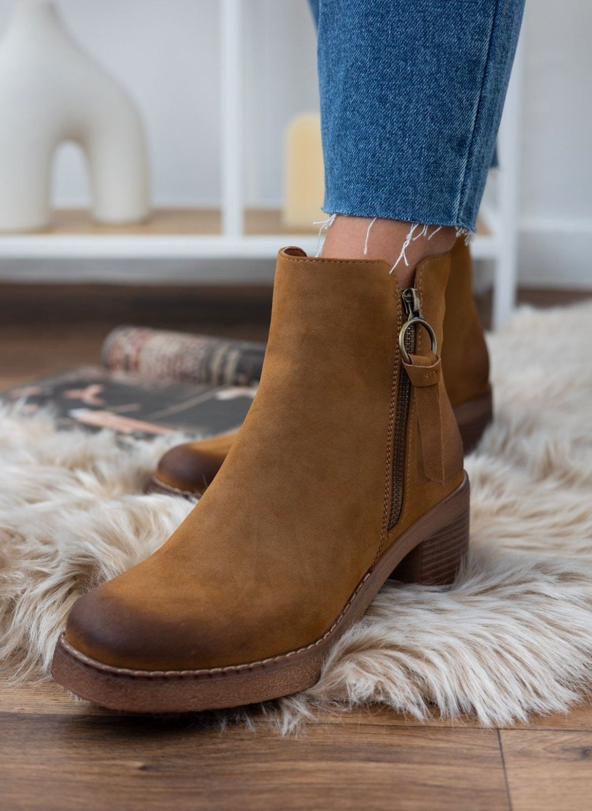Camel suede ankle boot with side zipper and block heel, worn on model on a fluffy white rug