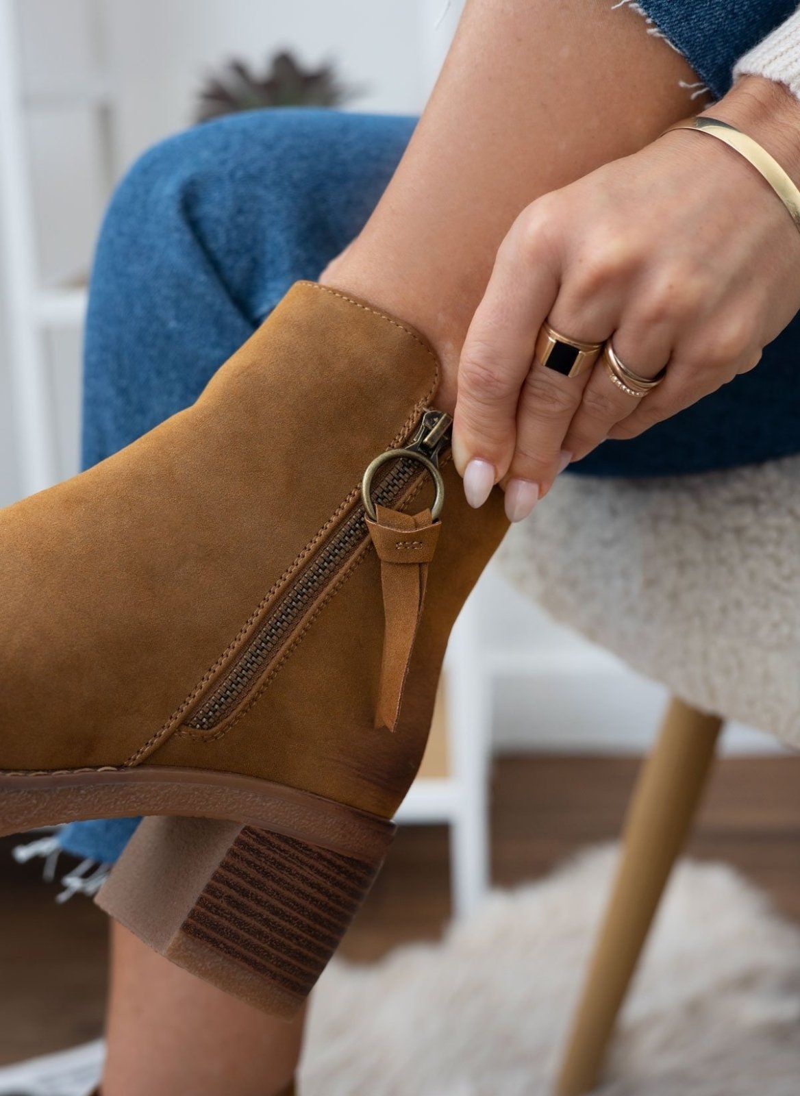 Model fastening the side zip of a camel suede ankle boot with stacked block heel, close-up detail
