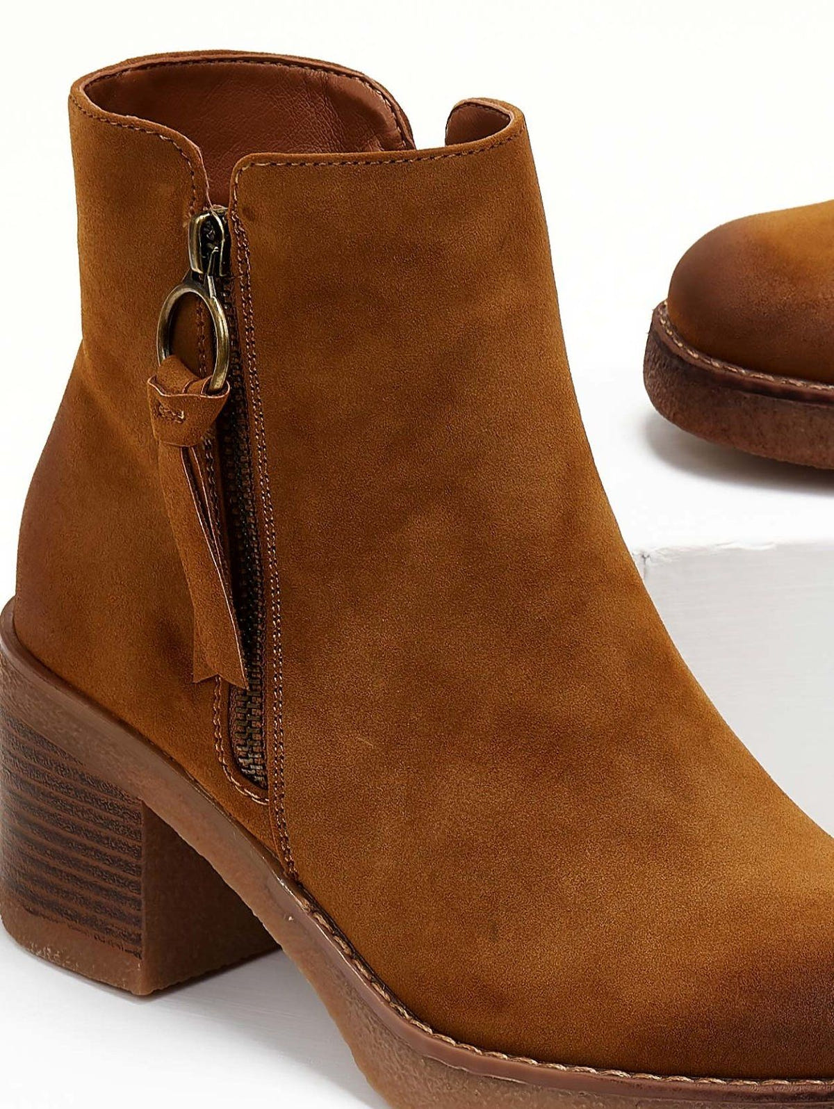 Close-up of the side zipper ring pull and tassel on a camel suede ankle boot with stacked block heel