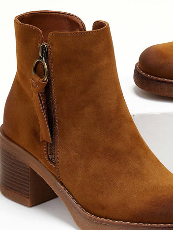 Close-up of the side zipper ring pull and tassel on a camel suede ankle boot with stacked block heel