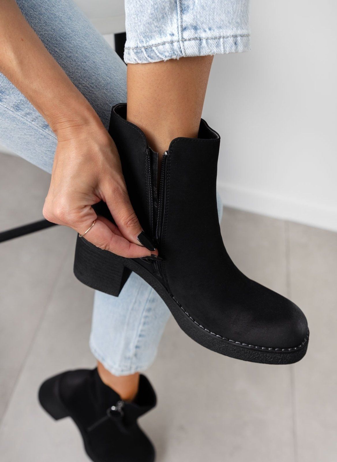 Model zipping up a black nubuck ankle boot with chunky block heel, close-up of the side zipper