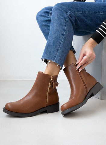 Tan ankle boots with gold metal zipper and black sole, worn on model, seated side view