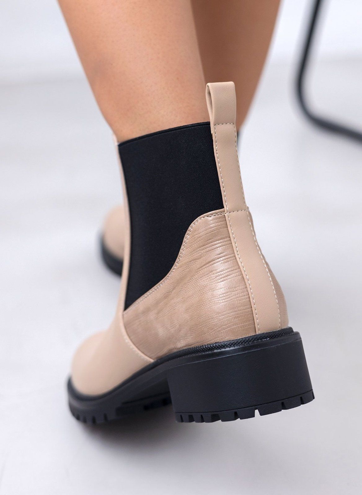 Beige Chelsea boot with black elastic gusset, embossed heel counter and pull tab, worn on model, back view