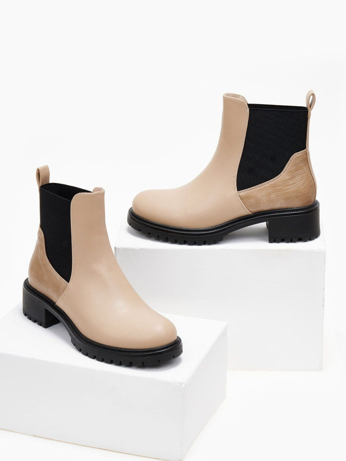 Pair of beige Chelsea ankle boots with black elastic panels and black lug soles, displayed on white blocks