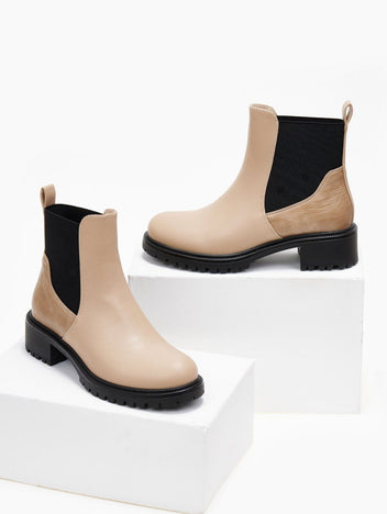 Pair of beige Chelsea ankle boots with black elastic panels and black lug soles, displayed on white blocks