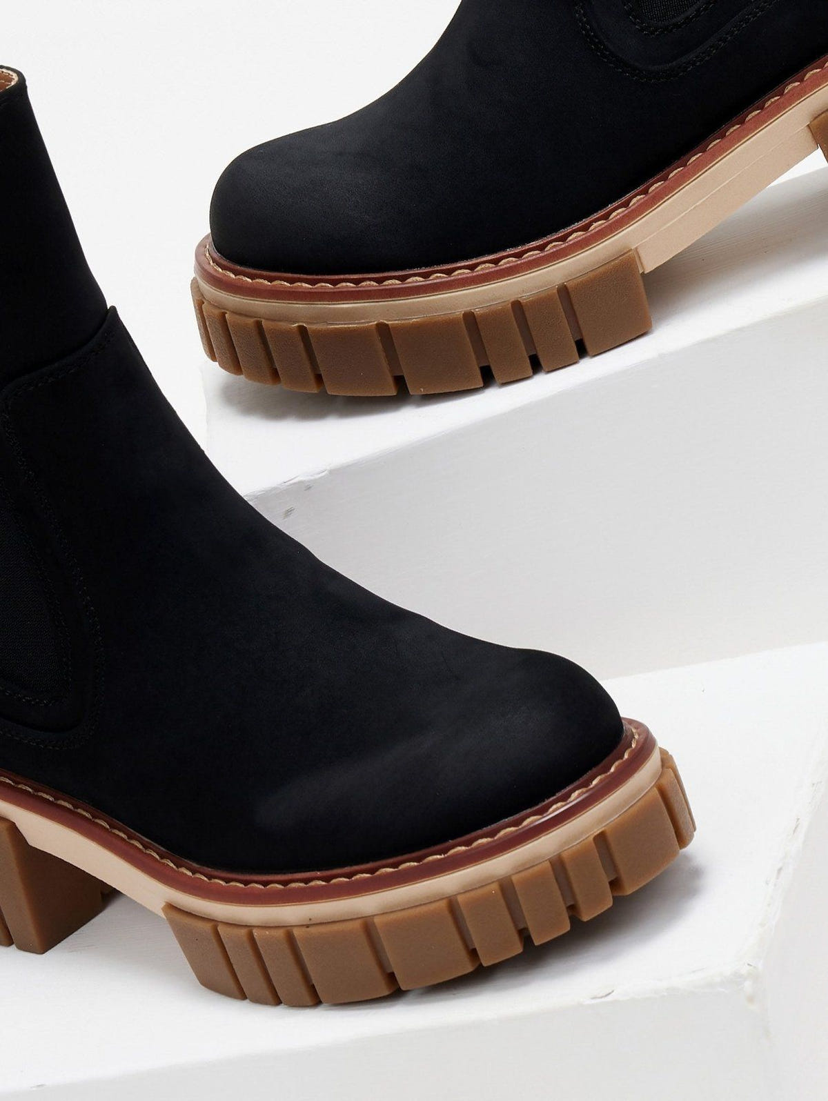 Close-up of black suede Chelsea boot toe with contrast stitching and chunky ridged tan platform sole