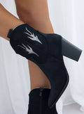 Black suede cowboy ankle boots with silver flame appliques and block heel, worn on model, side view